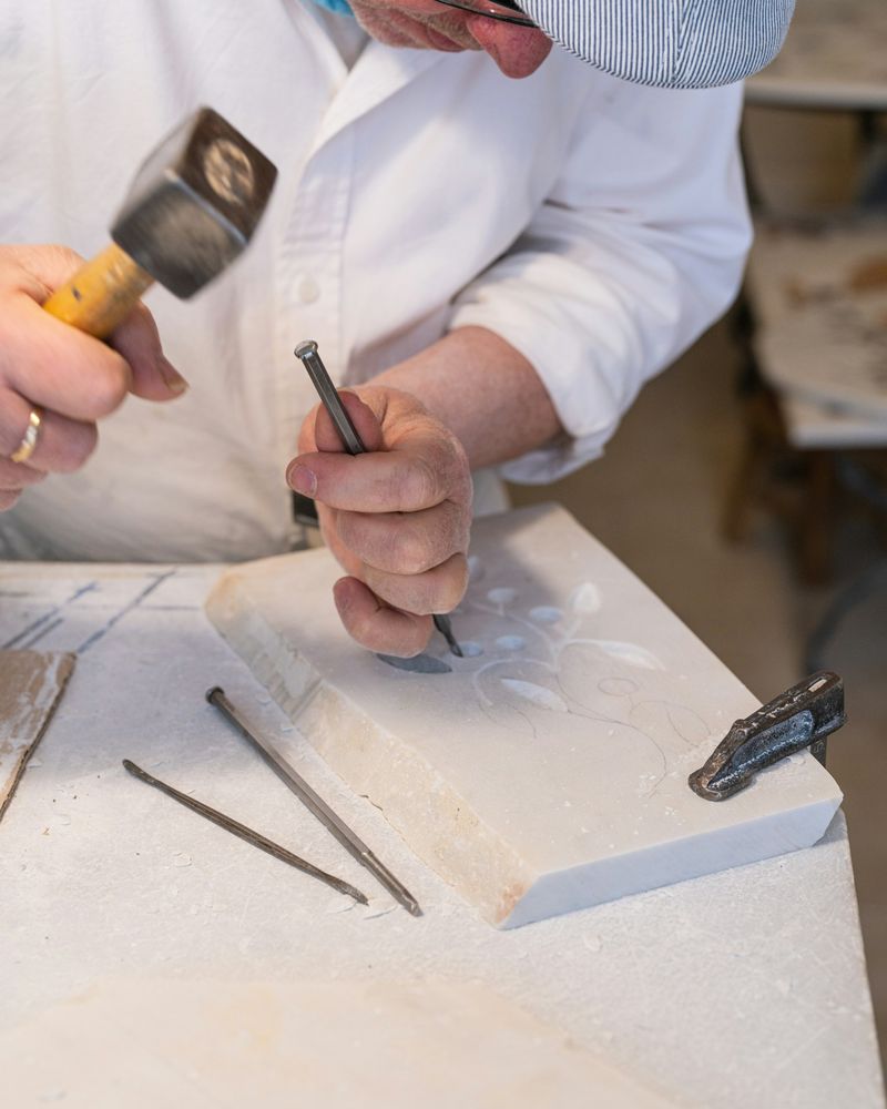 Hands guiding a chisel across a white marble slab at the workbench